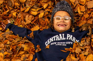 a child wearing a navy blue Central Park 1858 hoodie plays in fall leaves