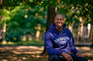 A man smiling and wearing a navy blue 1858 sweatshirt while sitting in Central Park