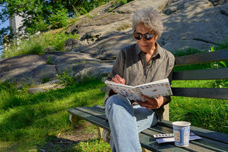 Person painting watercolors on a bench in a park with rocks and grass in the background