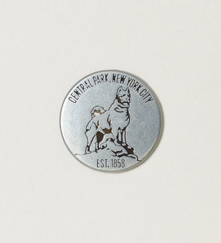 Close-up of a round silver collectible token featuring a dog statue with 'Central Park, New York City, Est. 1858' text on a white background.