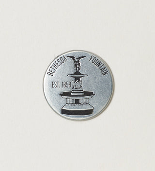 Close-up of a round silver token featuring Bethesda Fountain with 'Central Park, New York City, Est. 1858' text on a white background.