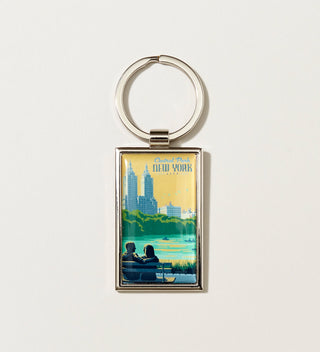 a silver metal keychain with  a  Travel Poster style artwork of two people sitting on a Central  Park bench