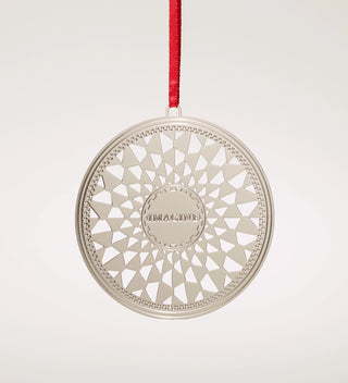 a stamped silver plated brass ornament hanging on a red ribbon with a grey background