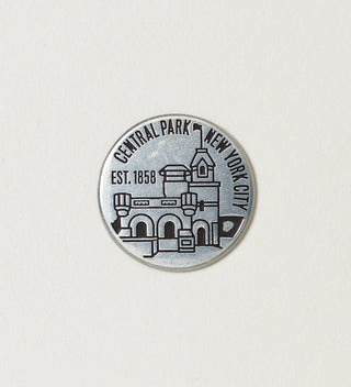 Close-up of a round silver token featuring Belvedere Castle with 'Central Park, New York City, Est. 1858' text on a white background.