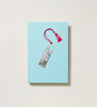 Bookmark with an Obelisk and tree blossom design featuring a rose pink tassel, placed on a closed blue  book on a white background.