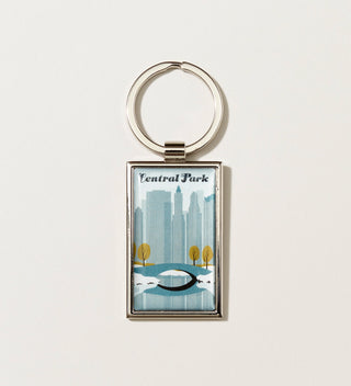  a silver key chain with a Travel Poster style artwork of a winter scene in Central Park with a bridge, trees and skyscrapers in the background