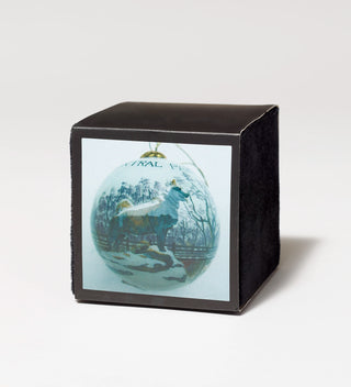 Decorative ornament with a painting of a dog standing on a rock in a winter scene, displayed in a black velvet box.