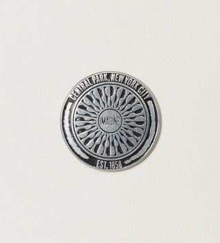 Close-up of a round silver token with 'Central Park, New York City, Est. 1858' text and the 'Imagine' mosaic design on a white background.