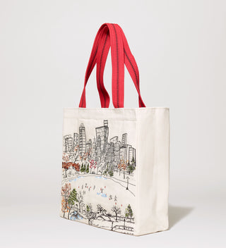 Side view of a white tote bag with red handles, featuring an embroidered scene of ice skaters at Central Park