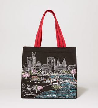 Black tote bag with a red handle, featuring an embroidered scene of people rowing boats in Central Park