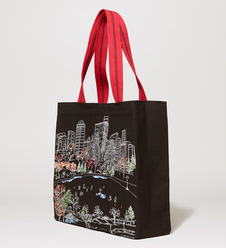 Side view of a black tote bag with red handles, featuring an embroidered scene of ice skaters at Central Park