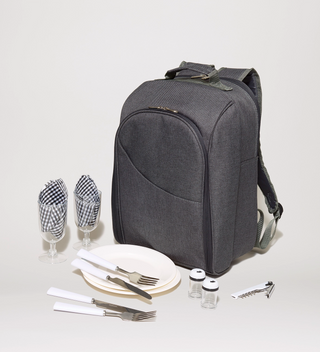 Gray picnic backpack, shown alongside cutlery, salt and pepper shakers, plates, glasses, napkins, and a bottle opener