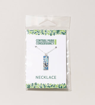 Packaged Central Park Conservancy necklace with a blue leaf design, displayed on a light grey background