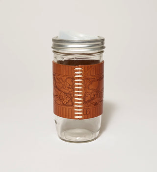 A stitched detail of a glass travel mug featuring a leather wrap embossed with a historical plan of Central Park and a drinking spout