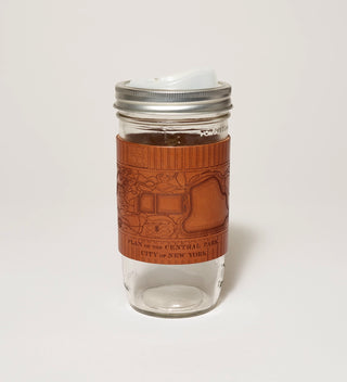 A glass travel  mug featuring a leather wrap embossed with a historical plan of Central Park and a   drinking spout