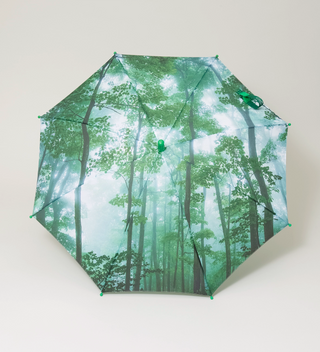 Fully open umbrella featuring a forest canopy design with green leaves and trees, viewed from above on a light grey background