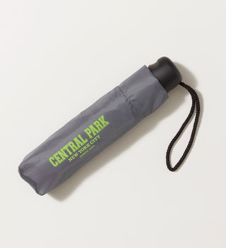 An closed grey umbrella with black handle in a grey sleeve with CENTRAL PARK New York City  Since 1858  printed in light green against a light grey background