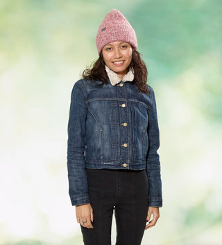 a smiling woman poses in a red and white marled yarn knit hat with woven wraparound tag that reads 'Central Park Est. 1858, NYC' in front of a dappled green background