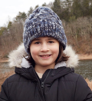 A happy child smiles while wearing a winter hat and a marled blue and white knit hat with a Central Park label.