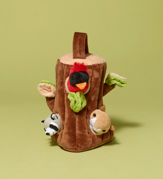 Plush toy shaped like a tree stump with a cardinal, a raccoon, and a chipmunk peeking out of it on a light green background.