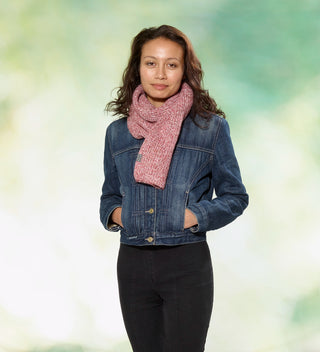 a model in a denim jacket wears  red and white mélange knit scarf with a grey tag that reads Central Park  since 1858 against a dappled green background