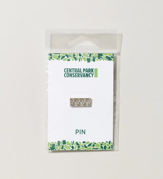 a packaged metal pin with incised spiral shapes and the Conservancy logo on a grey backgorund