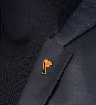 Detail photograph of an enamel and gold tone metal pin of Christo's The Gates on a black jacket lapel. 