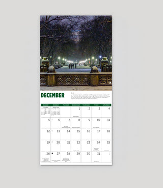 A vertical December calendar page featuring a winter scene on the Mall in Central Park with illuminated trees and a bridge above a white monthly calendar grid with green headers.