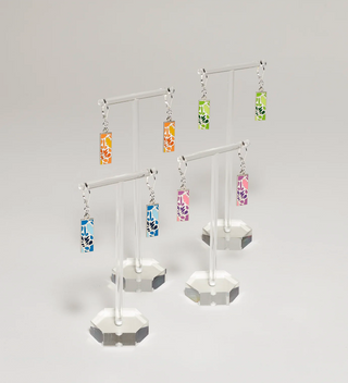 Four pairs of earrings with leaf design pendants in various colors (orange, blue, green, pink) displayed on clear stands