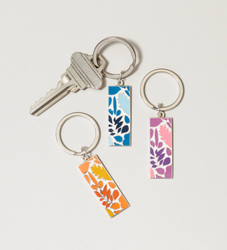 Three keychains with leaf design pendants in blue, pink, and orange, displayed with a key