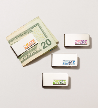 Three money clips with leaf design pendants in different colors (orange, pink, blue) and one money clip holding a twenty-dollar bill