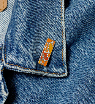 Central Park Conservancy pin with an orange leaf design, displayed on the collar of a denim jacket