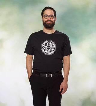 Man wearing a black t-shirt with a circular 'Imagine' mosaic design, inspired by John Lennon, standing with his hands in his pockets.