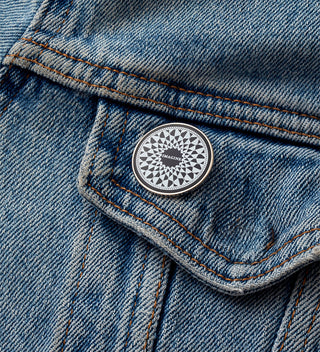 Close-up of a black and white round pin with a mosaic design and the word 'Imagine' in the center, on a blue jean jacket.