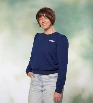 Woman posing in a navy quilted shirt with a small Central Park Conservancy logo on it 