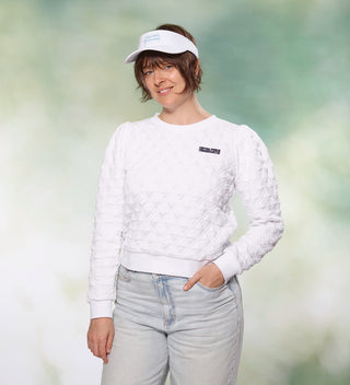 Woman posing in a white quilted shirt with a small Central Park Conservancy logo on it and white visor with a Central Park bench