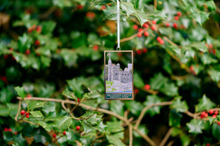 Decorative ornament with a castle design hanging on holly leaves with red berries.