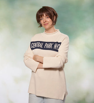 Woman with  arms crossed in cream colored roll neck sweater with Central Park NYC  on front in Navy blue