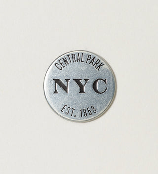 Close-up of the back of a round silver token with 'Central Park NYC, Est. 1858' text on a white background.