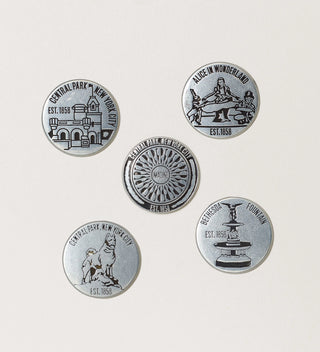 Collection of round tokens featuring Central Park landmarks  including a castle, Imagine mosaic, Balto, Fountain and 'Central Park NYC, Est. 1858' text on a grey background.