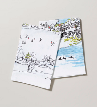 two folded tea towels featuring watercolor designs of winter skating and summer rowing in Central park 