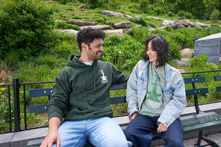 Two people sitting on a bench in Central Park with greenery and rocks in the background near the Davis Center.