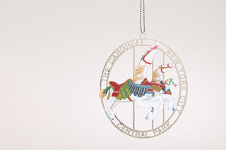 a stamped silver plated brass ornament in a design inspired by the Central Park Carousel hangs against a grey background.