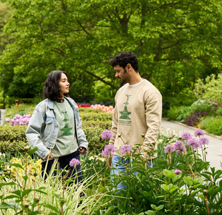 Two people standing in Conservatory Garden in Central Park with flowers and greenery wearing a tshirt and sweatshirt printed with an image of Bethesda Fountain