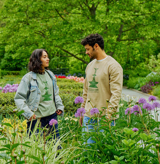 Two people standing in Conservatory Garden in Central Park with flowers and greenery wearing a tshirt and sweatshirt printed with an image of Bethesda Fountain