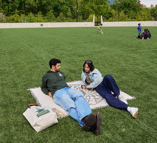 Two people sitting on a blanket at the Davis Center in Central Park NYC with a child playing in the background.