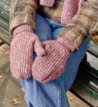 Close-up of red knit mittens on a woman's hands resting on her lap in Central Park, wearing blue jeans and a brown jacket. Mittens and scarf available a Central Park Conservancy Shop.