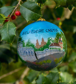 Hand-painted glass ornament showcasing Belvedere Castle in Central Park with a scenic backdrop of trees and architecture. All products available through Central Park Conservancy Shop