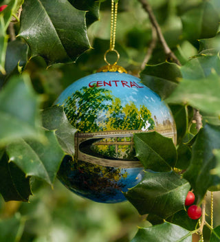 Hand-painted glass ornament illustrating Bow Bridge in Central Park, surrounded by scenic greenery. All products available through Central Park Conservancy Shop