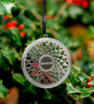 Decorative silver ornament with 'Imagine' text on a green leafy background